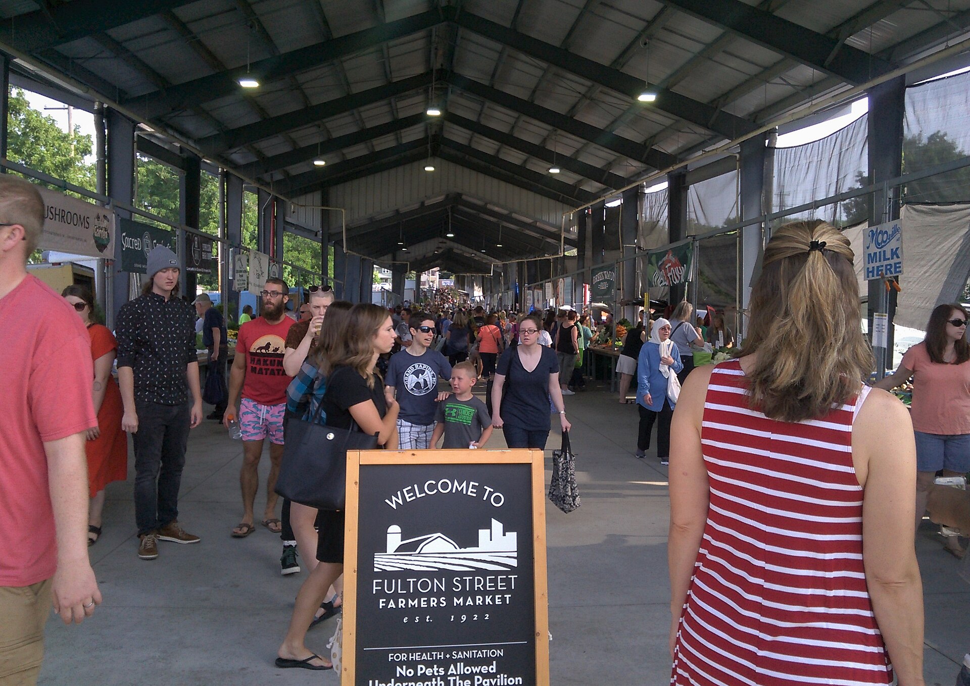 Vendor stalls and shoppers under the open-air sheds at the Fulton Street Farmers Market in Grand Rapids, Michigan